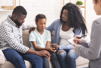 Worried mother sitting on couch with sad depressed kid and talking to counseling therapist.
