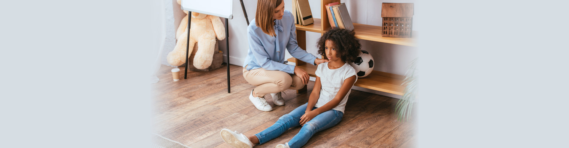 Psychologist touching shoulder of upset african american girl sitting on floor in office